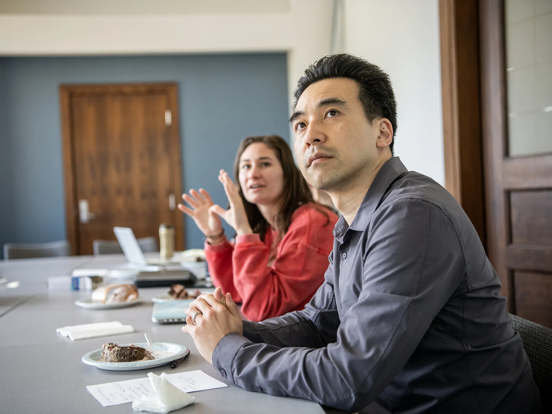 Kentaro Fujita, an Asian man, focuses on a slide show being shown out of the photo frame, as a student, a young white woman with long hair, next to him gestures as she explains a point of her project.