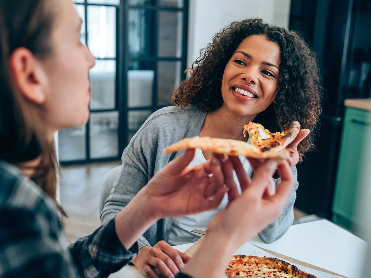 Two young women seated at a table enjoying a pizza