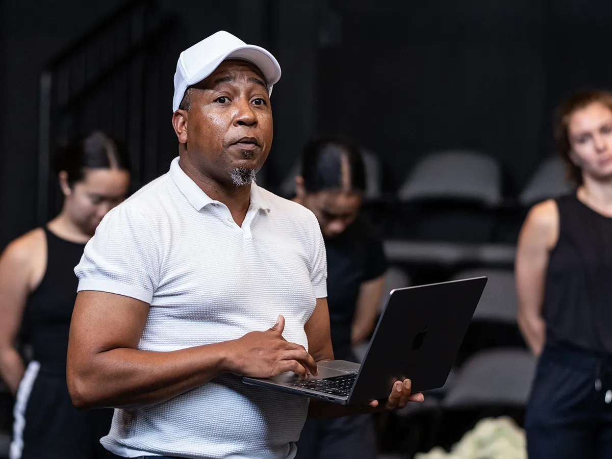 The choreographer of the class and chair of Ohio State’s Department of Dance, Charles Anderson, talks to the audience as his dancers stand in a line behind him. They’re dressed in black; his white shirt, gym shoes and ballcap stand out in the darkened theatre. He gestures and holds a laptop.