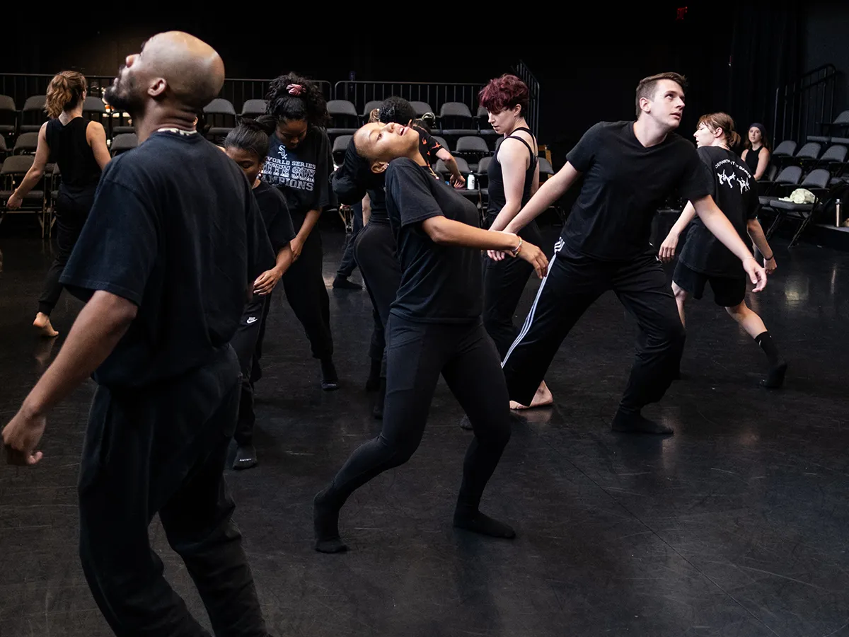 A mass of dancers shake and twitch as if being brought to life out of the cosmos and animated for the first time. Light shines on a male dancer as he steps to the side.