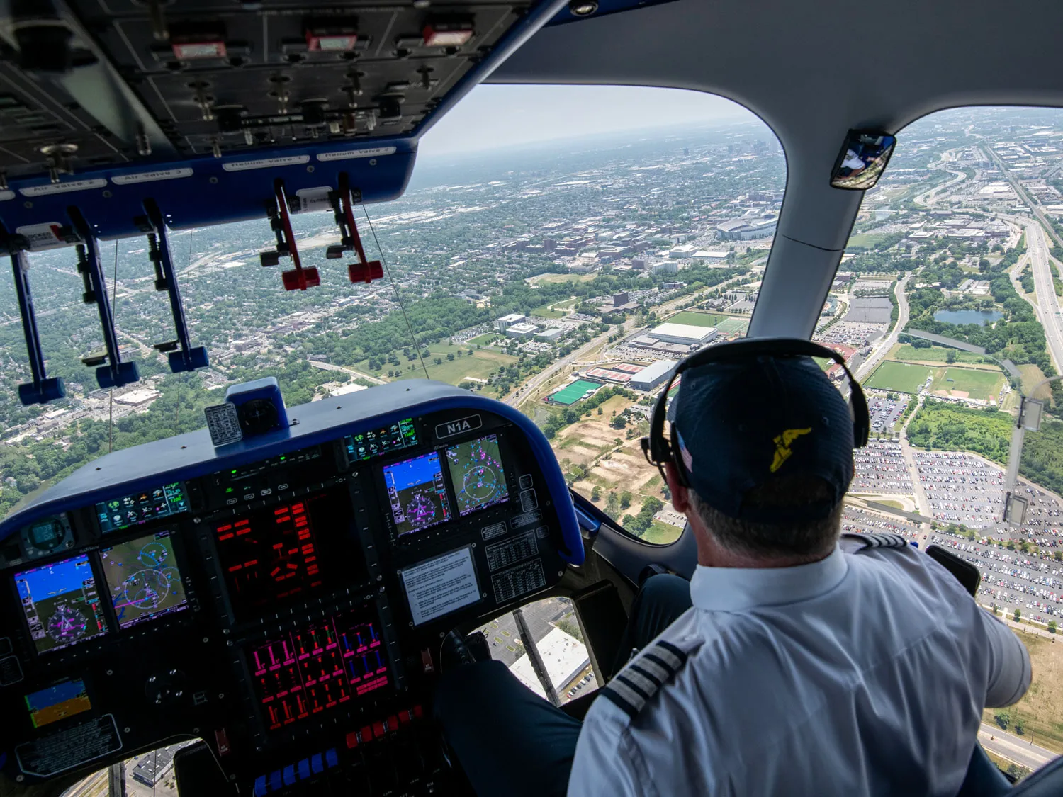 Pilot Joe Erbs looks out the cockpit window over the ground far below, where a highway, parking lots, buildings and fields can be seen.  