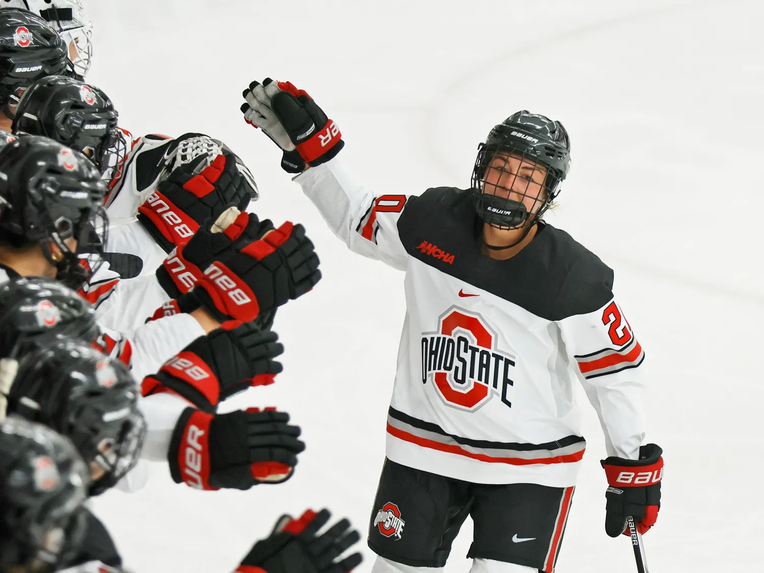 In her game uniform and helmet, Makenna Webster skates along a line of her ice hockey teammates giving high fives. 