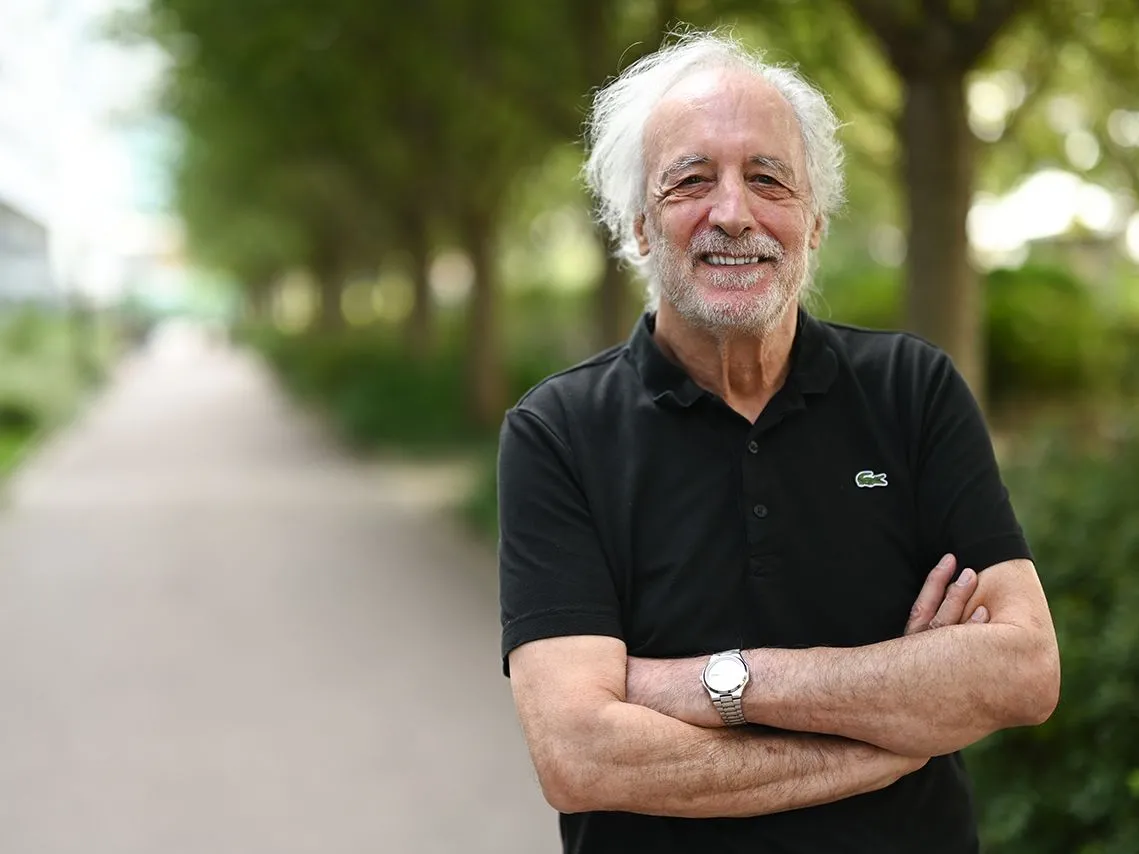 A white older man smiles as he poses for the photo, standing in front of a long walk lined with trees. It seems symbolic of the new fronts of knowledge he helped open up.