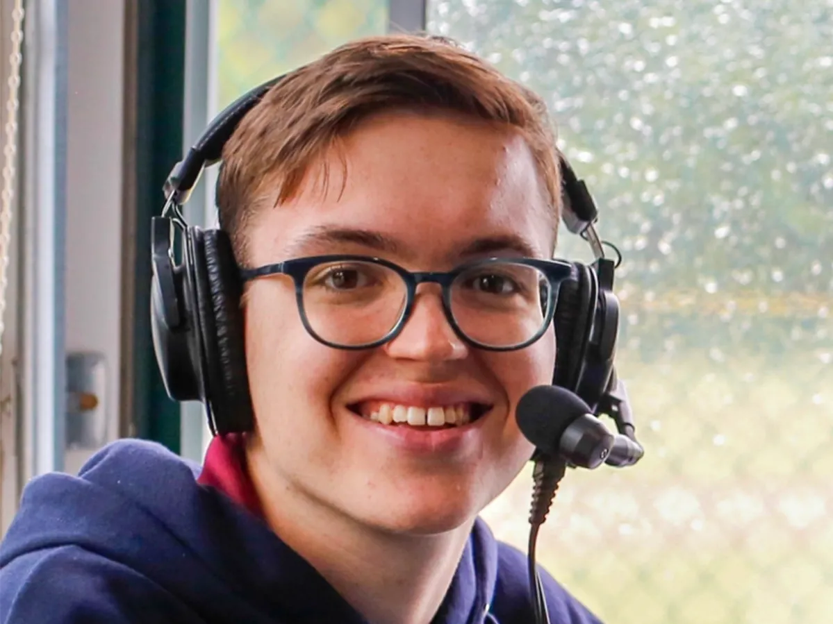 TYler Danburg, a young man with dark eyes and a friendly smile, wears a broadcast headset.