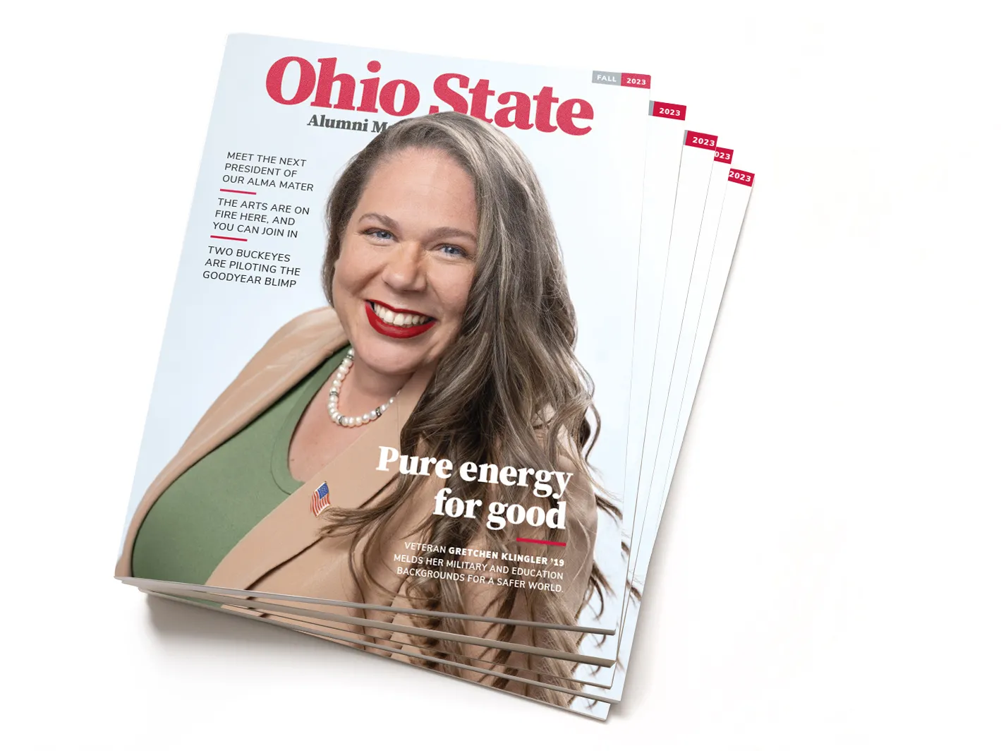 This photo shows a stack of Fall 2023 editions of Ohio State Alumni Magazine. The cover shows Gretchen Klinger, a smiling woman with long hair and bright lipstick wearing a business suit. She's leaning slightly toward the camera, as if getting ready to have a conversation with the reader or warmly greet them. The main headline says “Pure energy for good.”