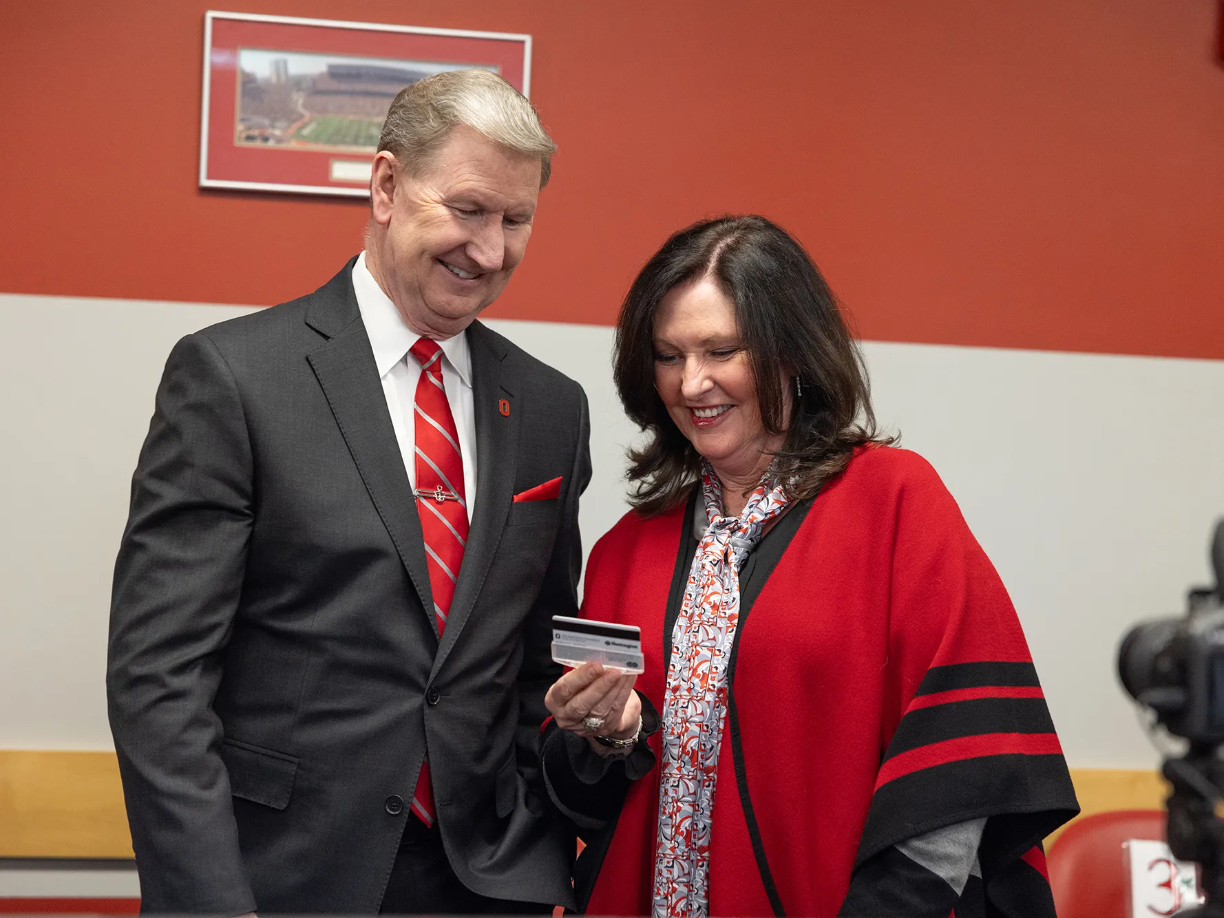 Ohio State President Ted Carter and his wife Lynda Carter smile as they look at her first BuckID in the office where Buckeyes have their ID photos taken. They’re both dressed up in Ohio State colors.