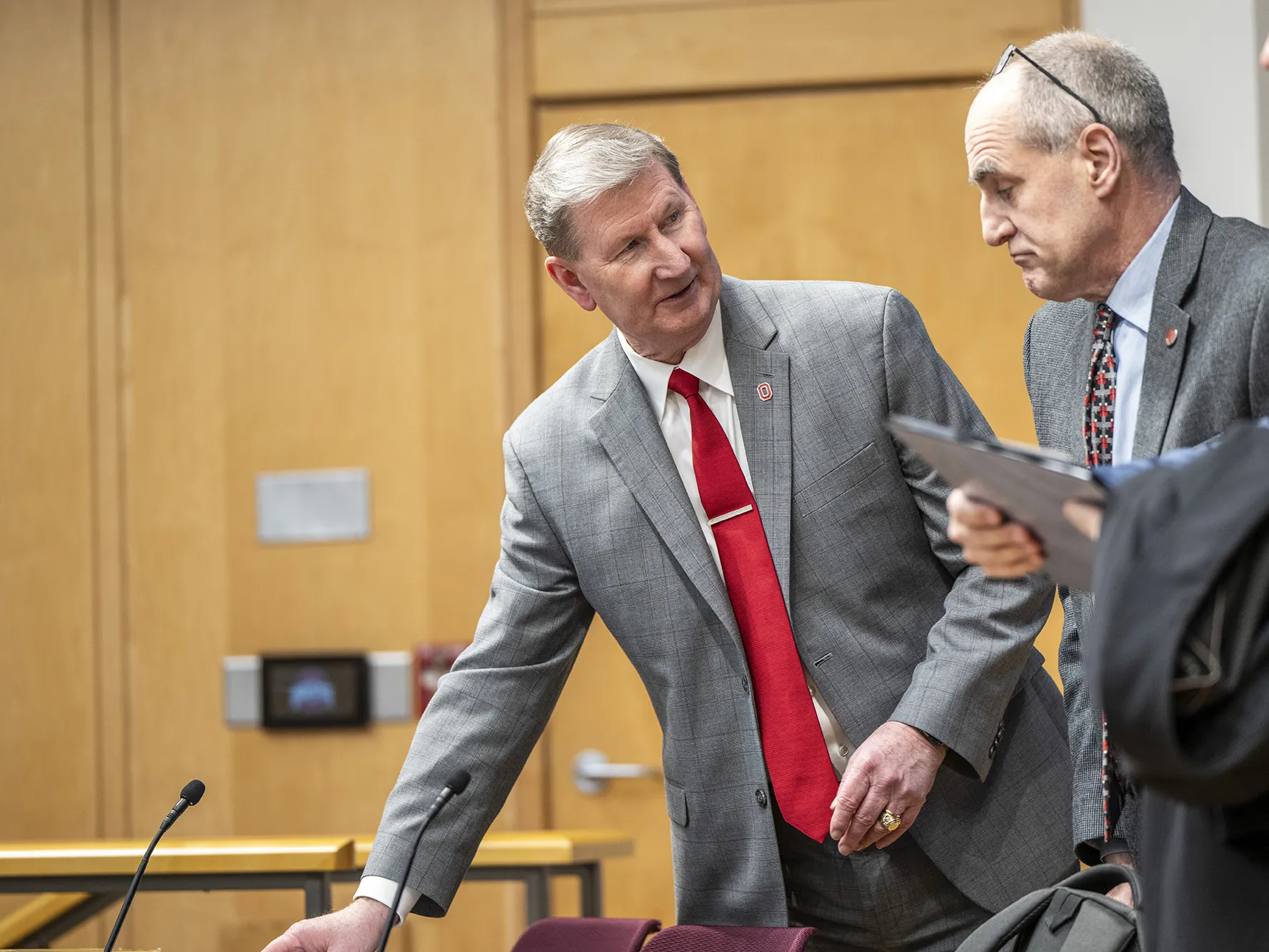 President Carter leans sideways to place something on a table as he looks the opposite way, toward the man standing next to him, Associate Professor Ben Givens. They’re chatting; Carter smiles and Givens has a furrowed brow. Both men wear similarly colored suits, and Givens wears his glasses pushed on top of his head.  