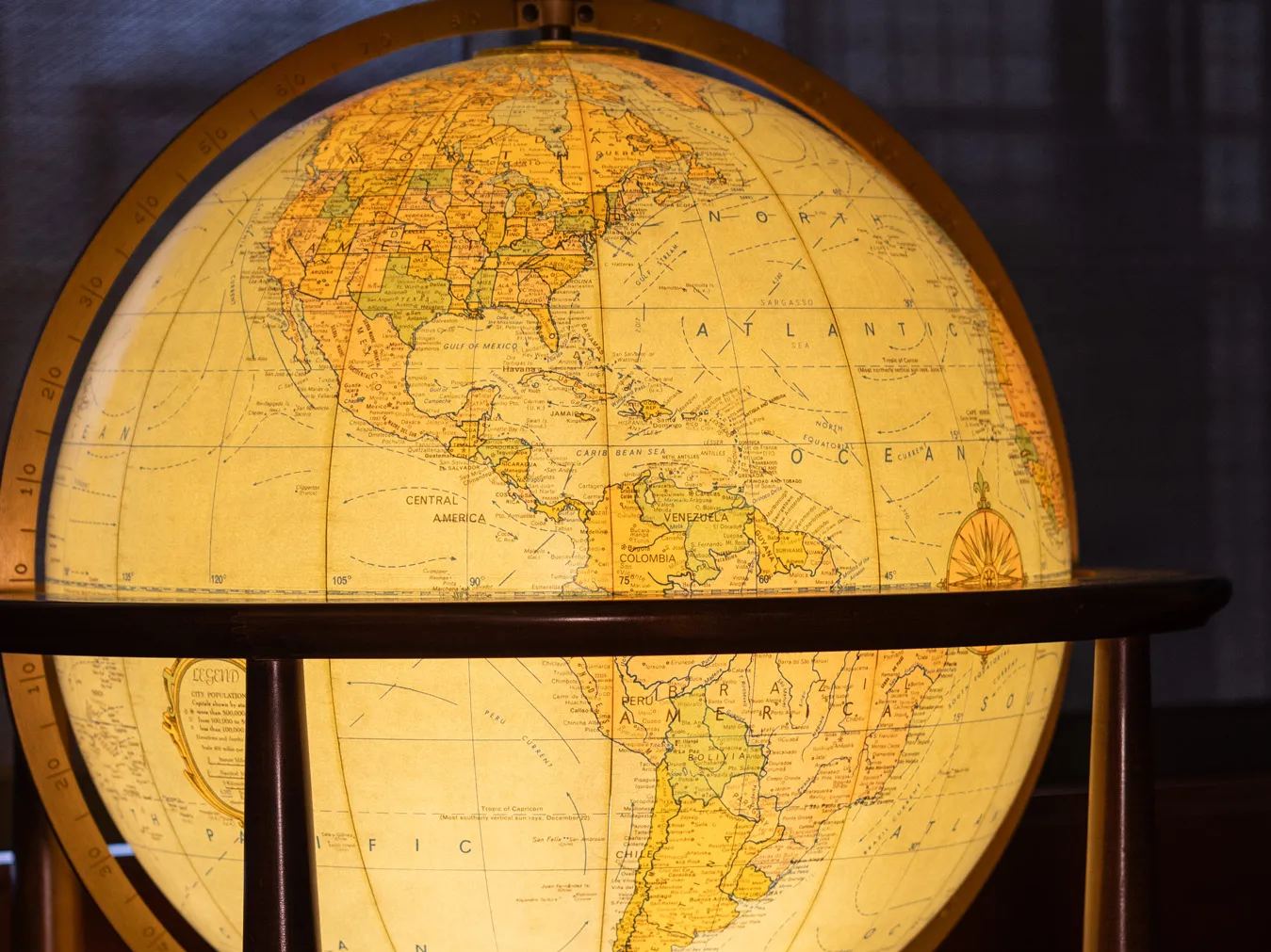 A lighted-up globe, positioned to show North and South America is held in a simple wooden stand. They background of the photo is dark, so the globe shines brightly.