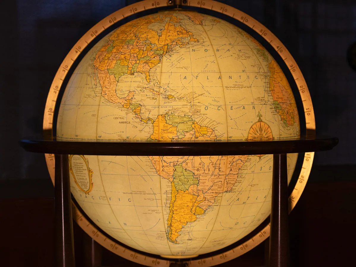 A lighted-up globe, positioned to show North and South America is held in a simple wooden stand. They background of the photo is dark, so the globe shines brightly.