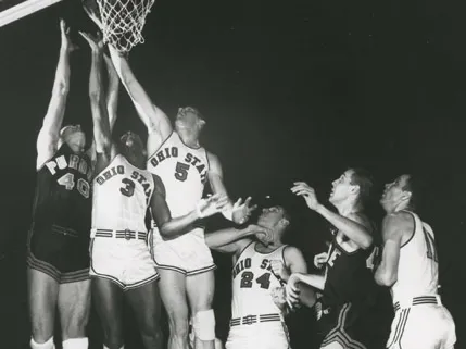 In a 1960 basketball game, three players jump high off the court to lay up and block a shot. Three more players on the ground box out opponents or prepare in case there’s the chance to rebound. Four of the six are Ohio State players—the others are from Purdue. Five of the six are white men; one Ohio State player is black. They’re all tall and think and focused on the ball.