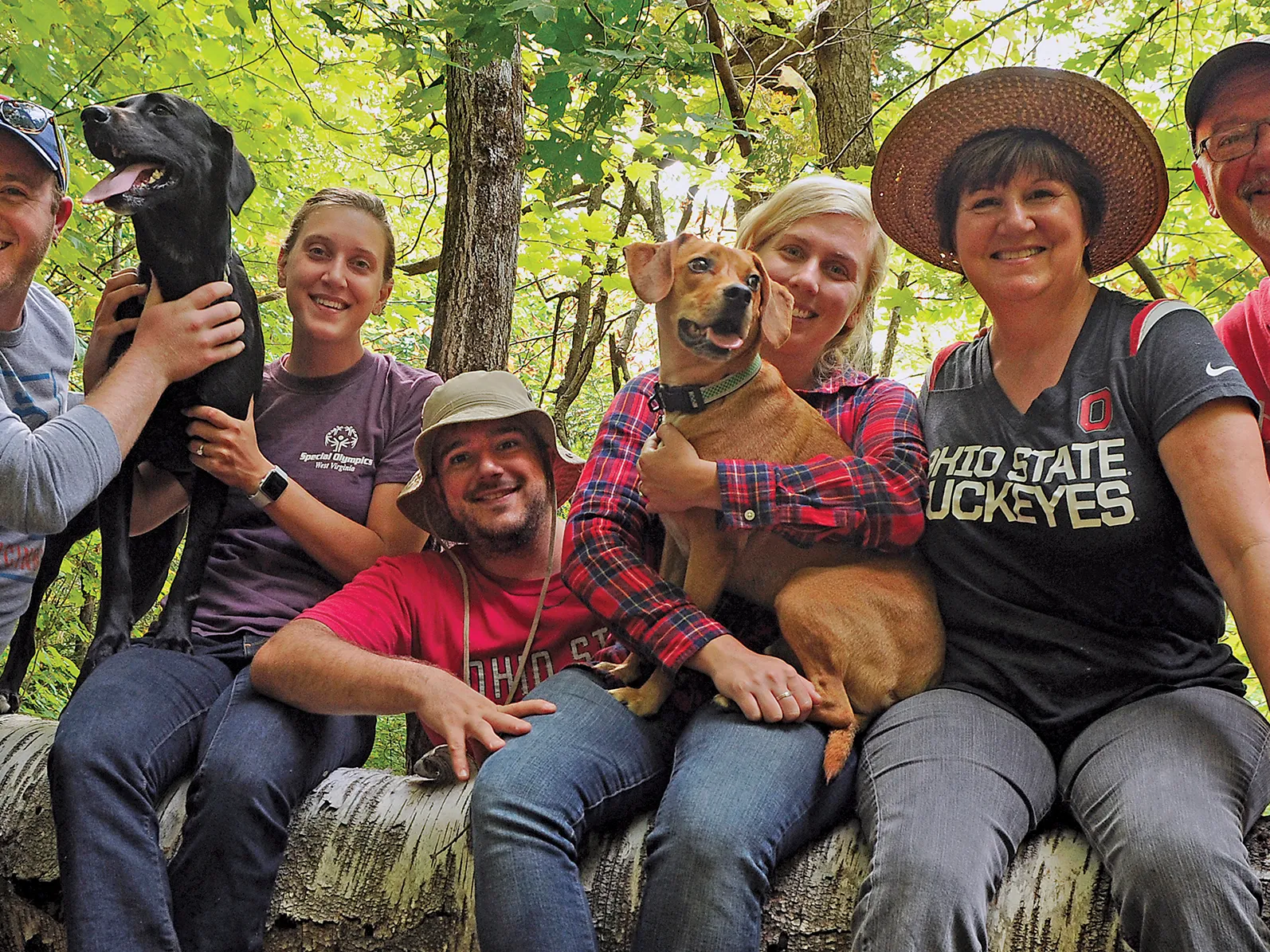 Sitting on a low wall on a hiking trail in the woods, Mary Alice Casey and her family pose with their pets. Both of her grown children and their spouses brought their dogs for their hike, and her husband, an alumnus, wears an Ohio State T-shirt. The whole family looks like they’re enjoying themselves.