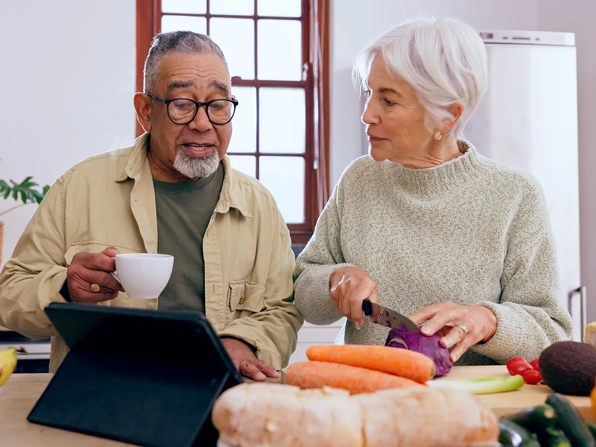 A senior couple prepares a healthy meal with a variety of vegetables and fruits in view