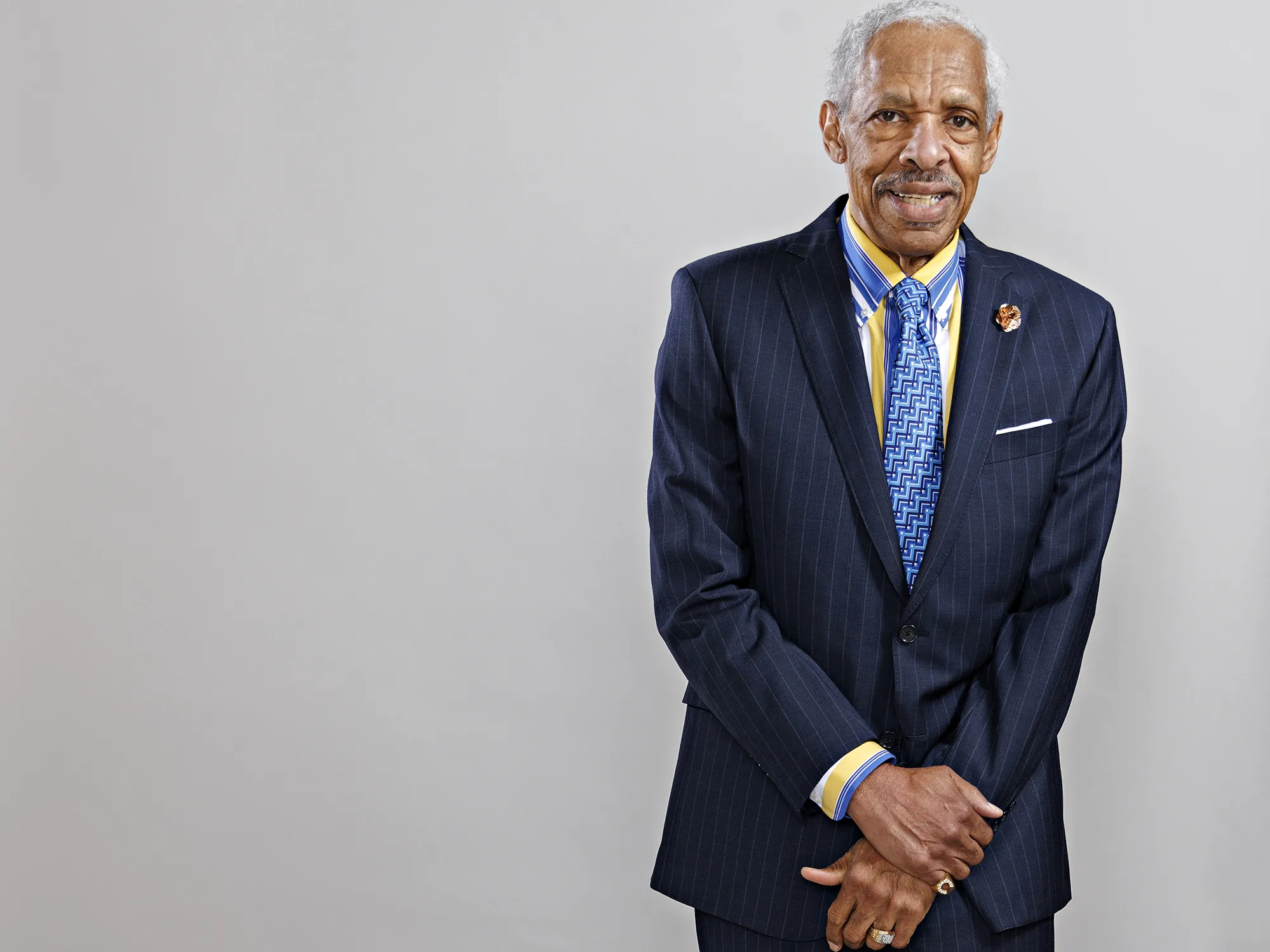 Leonard Haynes, an older Black gentleman with white hair wearing a suit, looks directly into the camera and smiles as if he’s listening to you.