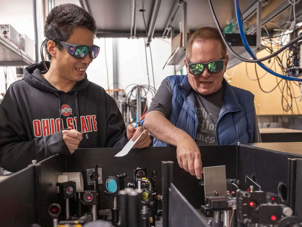 Lou DiMauro and a student, postdoc Yaguo Tang from China, wear safety glasses as they point out how a laser is split into two for their attosecond experiments to study electrons.