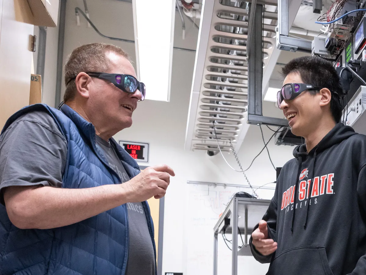 Lou DiMauro and a student, postdoc Yaguo Tang from China, wear safety glasses as they chat in the lab where they do their attosecond laser experiments to study electrons. They're both laughing as they talk.