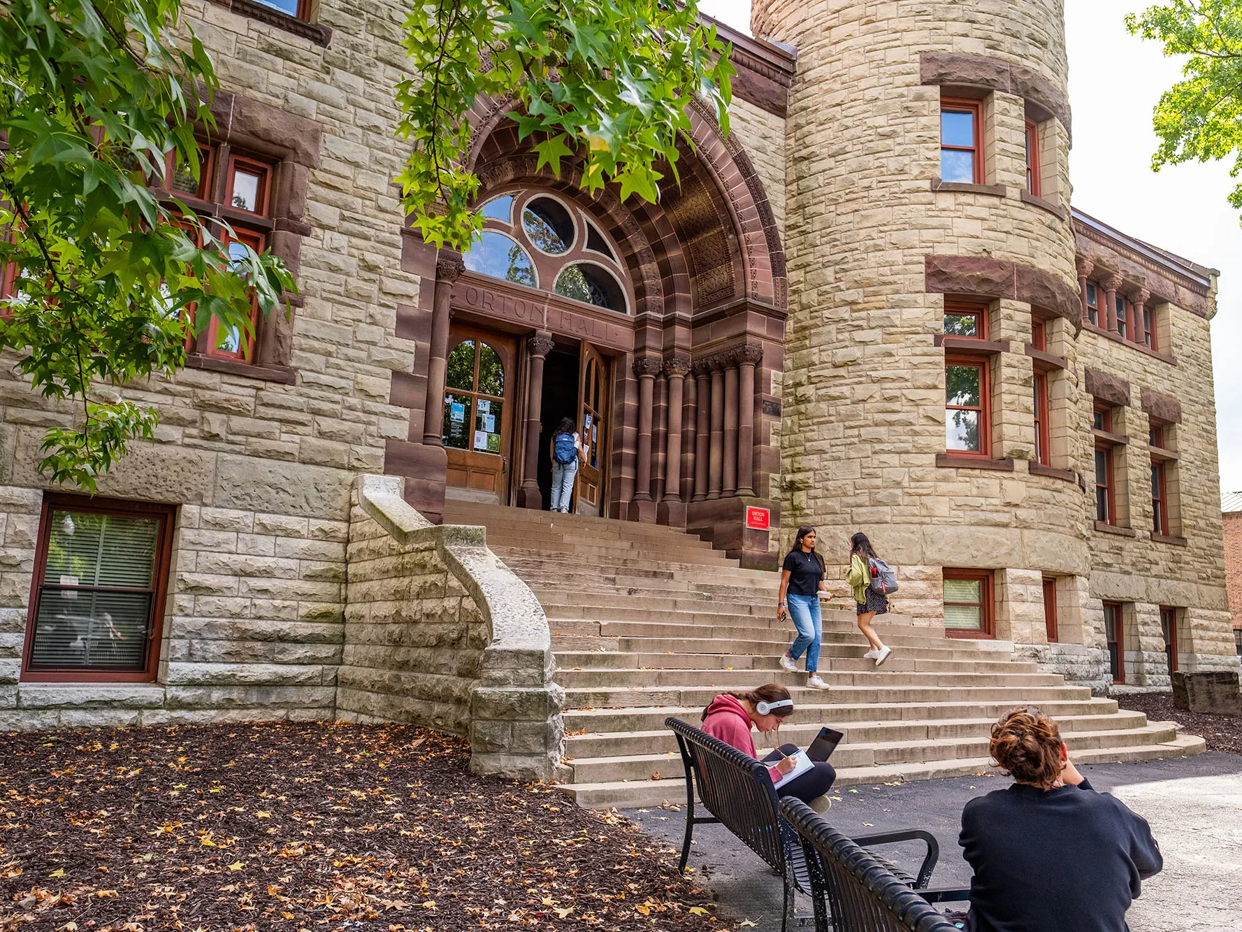 Orton hall is a stone building with 20 wide stone steps leading to the arched main entrance. The stone work is special and represents the different geological period of earth. Students walk in and out in this photo, which shows the stateliness of the building on a pretty day.