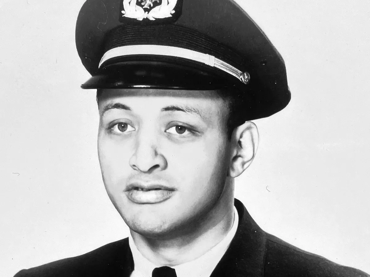 David Harris poses for an American Airlines headshot in a suit and narrow tie and pilot’s hat. He is a Black man and his expression says he is serious yet open or trustworthy—like someone you’d trust to fly your plane.