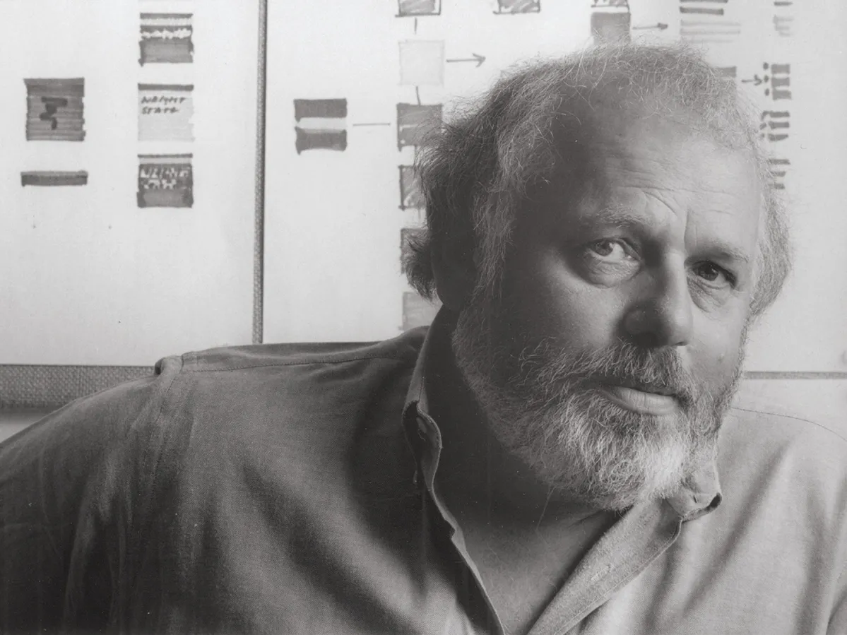 Peter Megert is shown in a portrait. He’s a white man with beard and wispy gray hair that hangs past his ears. He looks directly into the camera, appearing both serious and intellectual, but not in an unfriendly way.