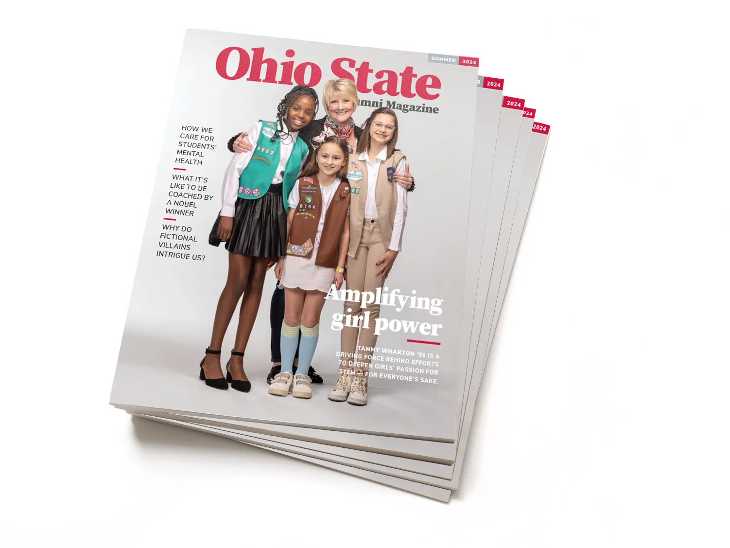 This is a stack of magazines. On the cover of the summer 2024 edition of Ohio State Alumni Magazine, Tammy Wharton, a white woman with short blond hair and a friendly smile, looks directly at the viewer while she has her arms wrapped around the Girl Scouts on either side of her. A third girl stands in front of her. The girls are all smiling, too, and dressed in their uniforms, they seem super pleased to be photographed with their leader.