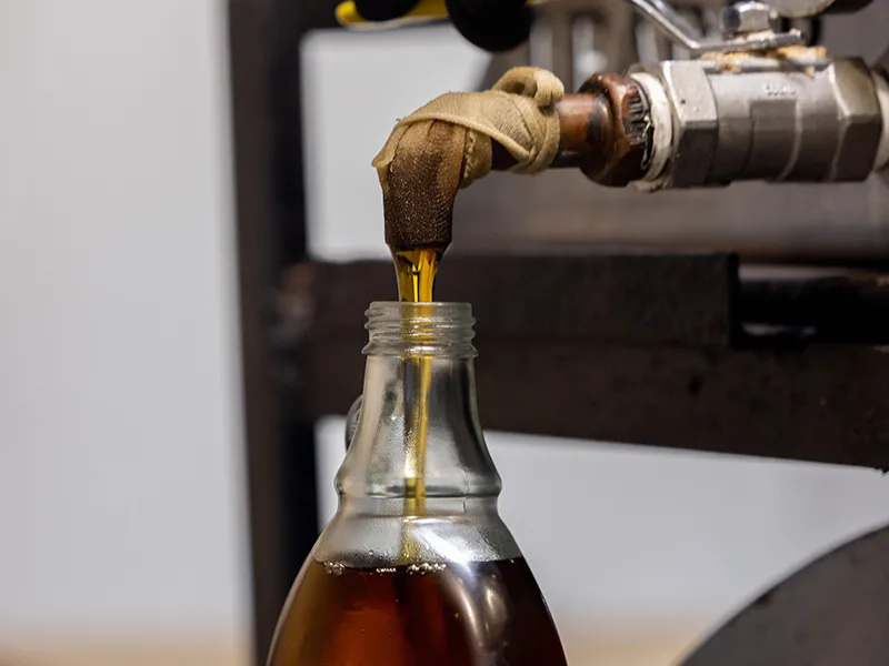 A glass bottle steams up as hot maple syrup is added from a metal spigot. The tank the spigot is attached to is not shown in this closeup photo.