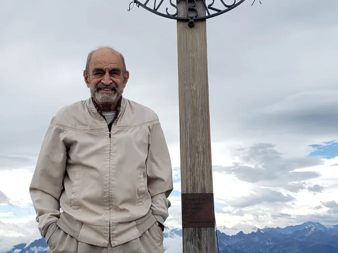 An older man with a friendly smile poses with his hands in his pockets while on Bergsohn Innsbruck, while on a ski hill in Austria. 