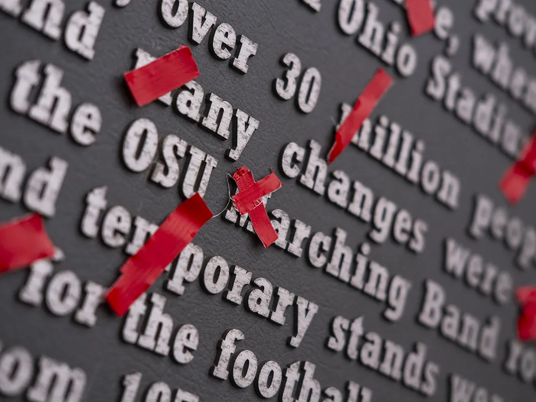 A gray plaque outside ohio stadium has every single m crossed out with bright scarlet tape.