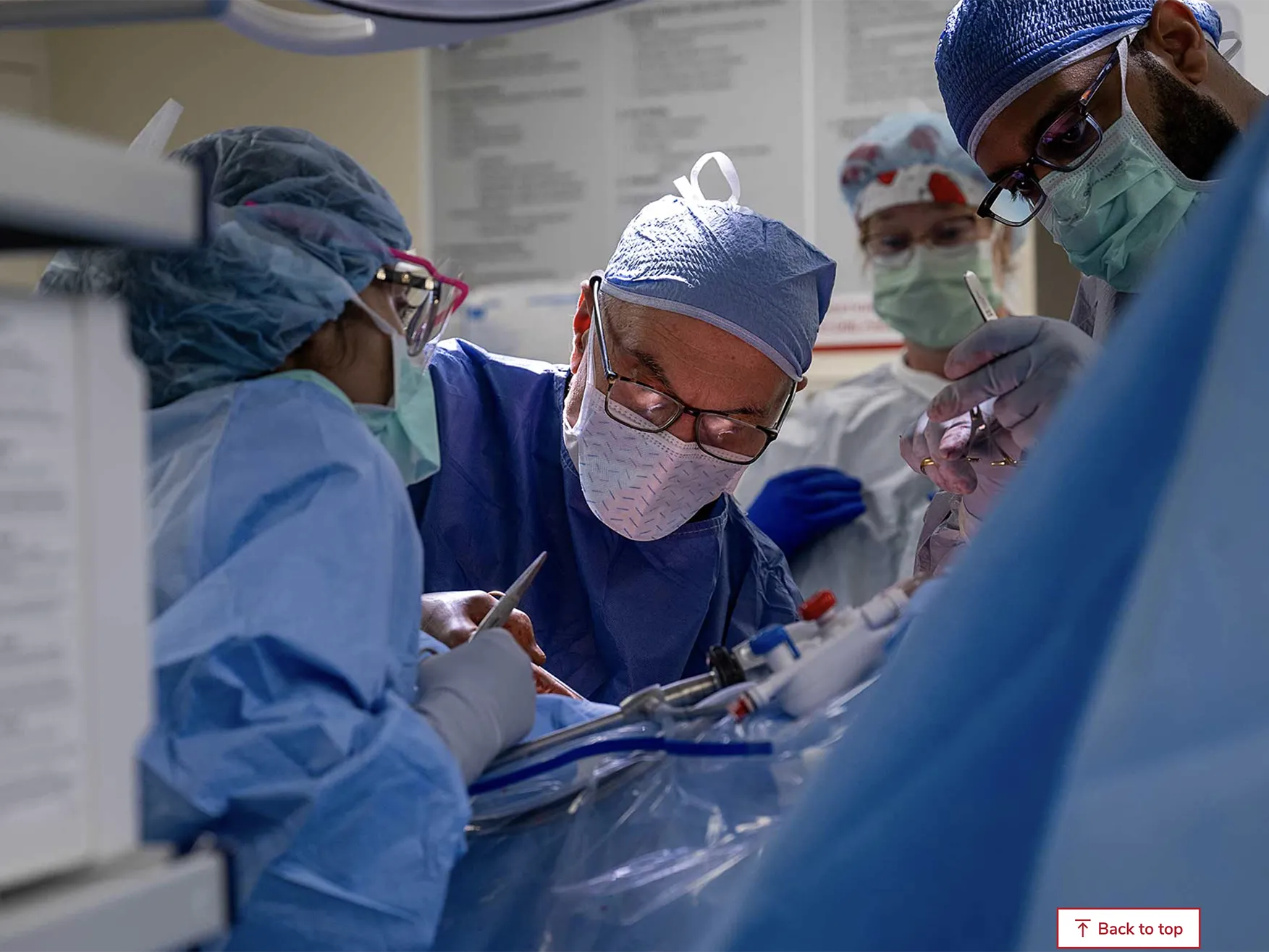 A team of Ohio State Wexner Medical Center employees works in the operating room to remove a donor&#039;s kidney. Ther are all suited up in scrubs, face masks and caps and lean over the patient, who cannot be seen.