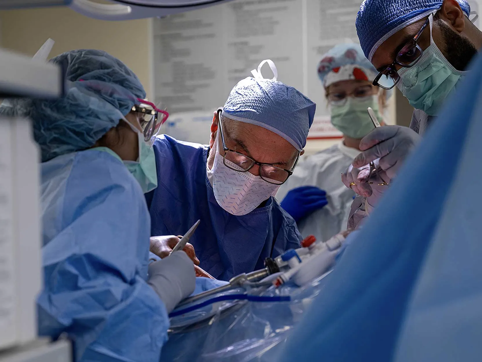 A team of Ohio State Wexner Medical Center employees works in the operating room to remove a donor&#039;s kidney. Ther are all suited up in scrubs, face masks and caps and lean over the patient, who cannot be seen.