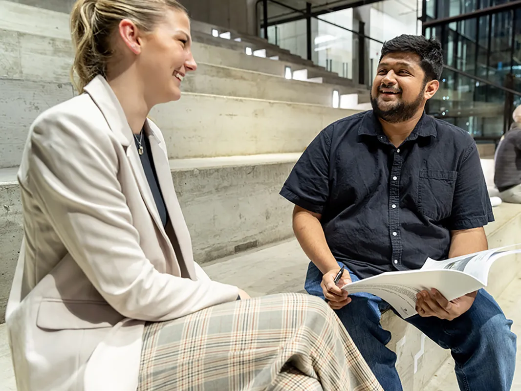 Andre Banerjee, a young Indian-Latino man, laughs as he sits on steps talking with a college student, who is also grinning. She's a young white woman wearing a suit and they are conducting a mock interview at Ohio State.