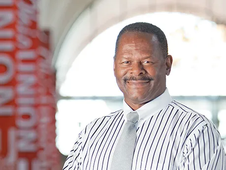 Dressed in a striped dress shirt, tie and dress pants, Moody smiles as he poses on the second floor of the student union