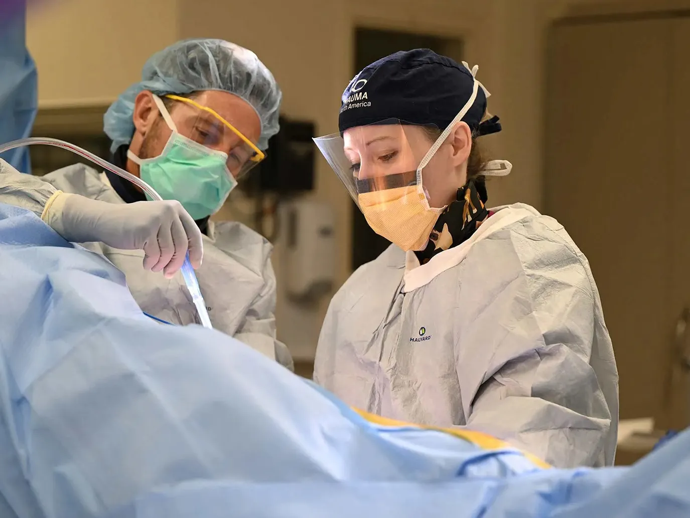 Orthopedic surgeon Angela Collins is covered in protective gear during a surgery in a hospital operating room. A man, similarly gowned-up, assists.