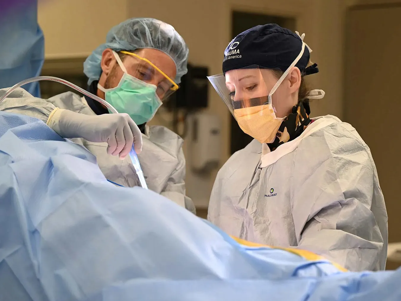 Orthopedic surgeon Angela Collins is covered in protective gear during a surgery in a hospital operating room. A man, similarly gowned-up, assists.