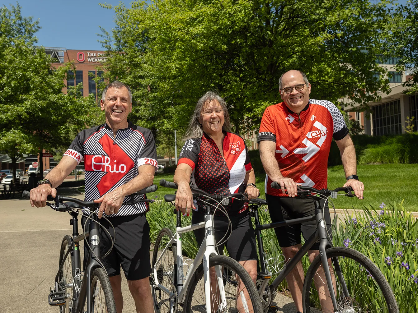 Three people in Ohio State bicycle jerseys pose for a photo with their bicycles. They&#039;re laughing and seem to be having a good time.