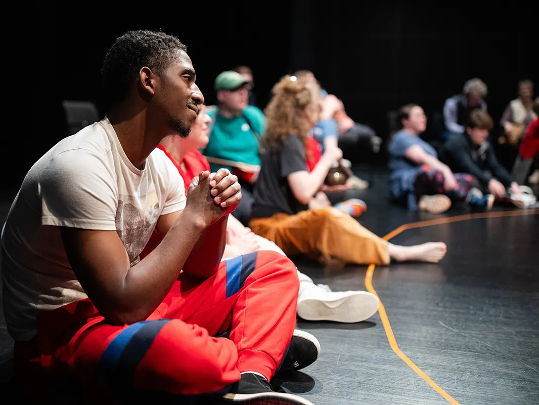Sitting on the floor of an auditorium in a big circle are a young Black man and others with autism, as well as ohio state students. They're getting ready to participate in a special Shakespeare and Autism program