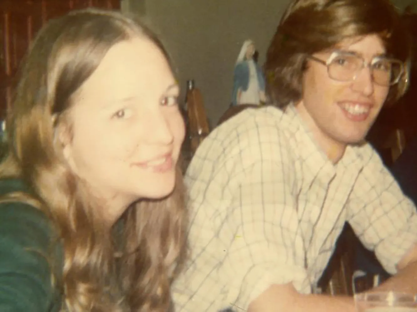In this 1970s photo, a young white couple smiles at the person taking the picture, almost as if they&#039;re saying &quot;if you really have to take this photo, go ahead.&quot; He wears glasses and she has long hair--their hair color almost matches.