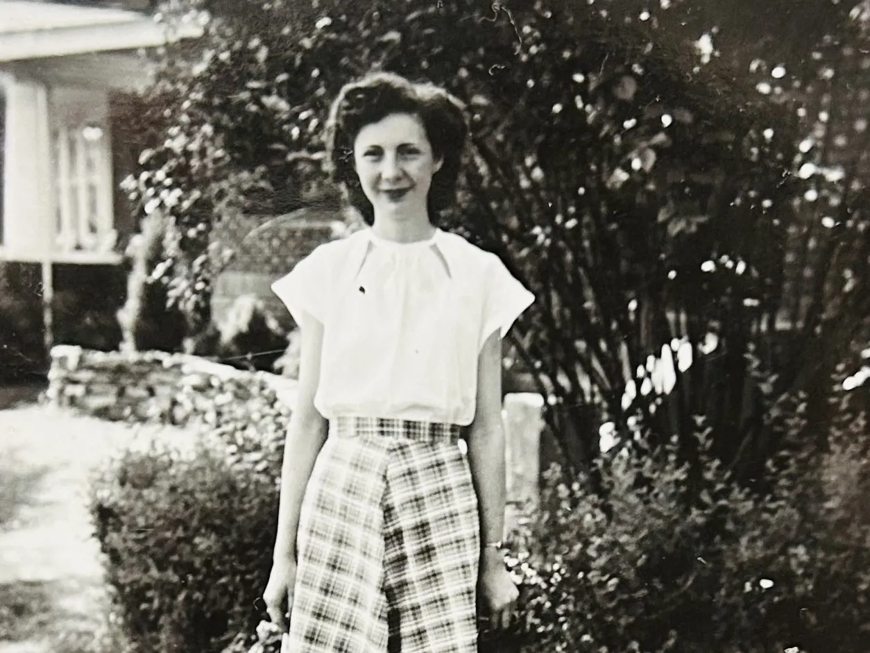 As a young woman in this black and white photo, Ruth Klingler McPheron stands in front of a house and greenery wearing a white blouse and shin-length plaid skirt. She is a white woman with a pretty hairstyle, a soft smile and the looks of someone you&#039;d want to tell stories to.