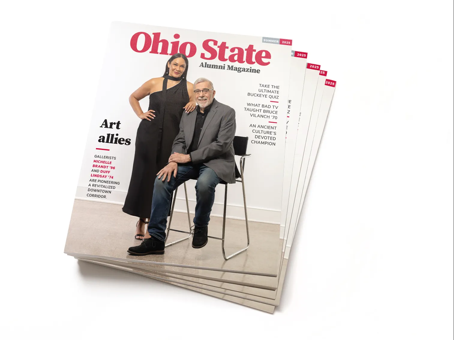 This is a stack of the Summer 2025 edition of Ohio State Alumni Magazine. The cover shows an older man sitting in a chair and a woman standing next to him, resting her arm on his shoulder. They seem comfortable with each other and elegant; both are dressed up. The woman has a knowing smile, a long black dress and scarf, and straight hair parted in the middle. She is Latina. The man wears a suit coat, jeans and a black button-down. He is white and has gray hair and beard and glasses.