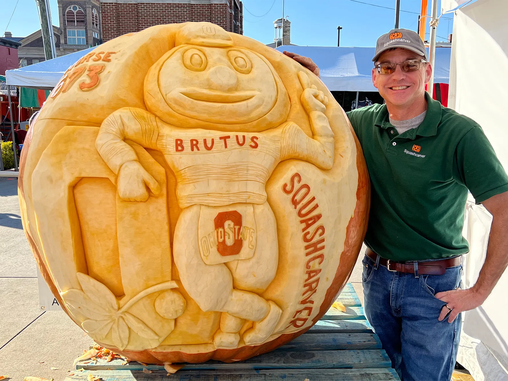 Gus Smithhisler grins as he shows off a giant pumpkin he just carved. It has Brutus Buckeye leaning on a Block O. Gus is a white man wearing sunglasses and a ballcap in this photo he shared.