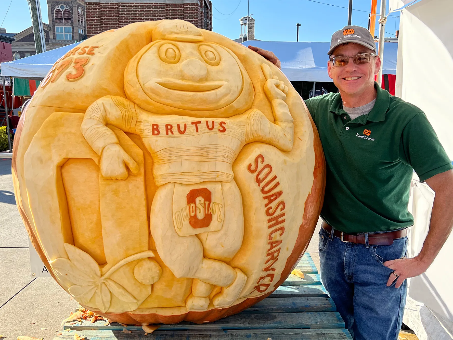 Gus Smithhisler grins as he shows off a giant pumpkin he just carved. It has Brutus Buckeye leaning on a Block O. Gus wears sunglasses and a ballcap in this photo he shared.