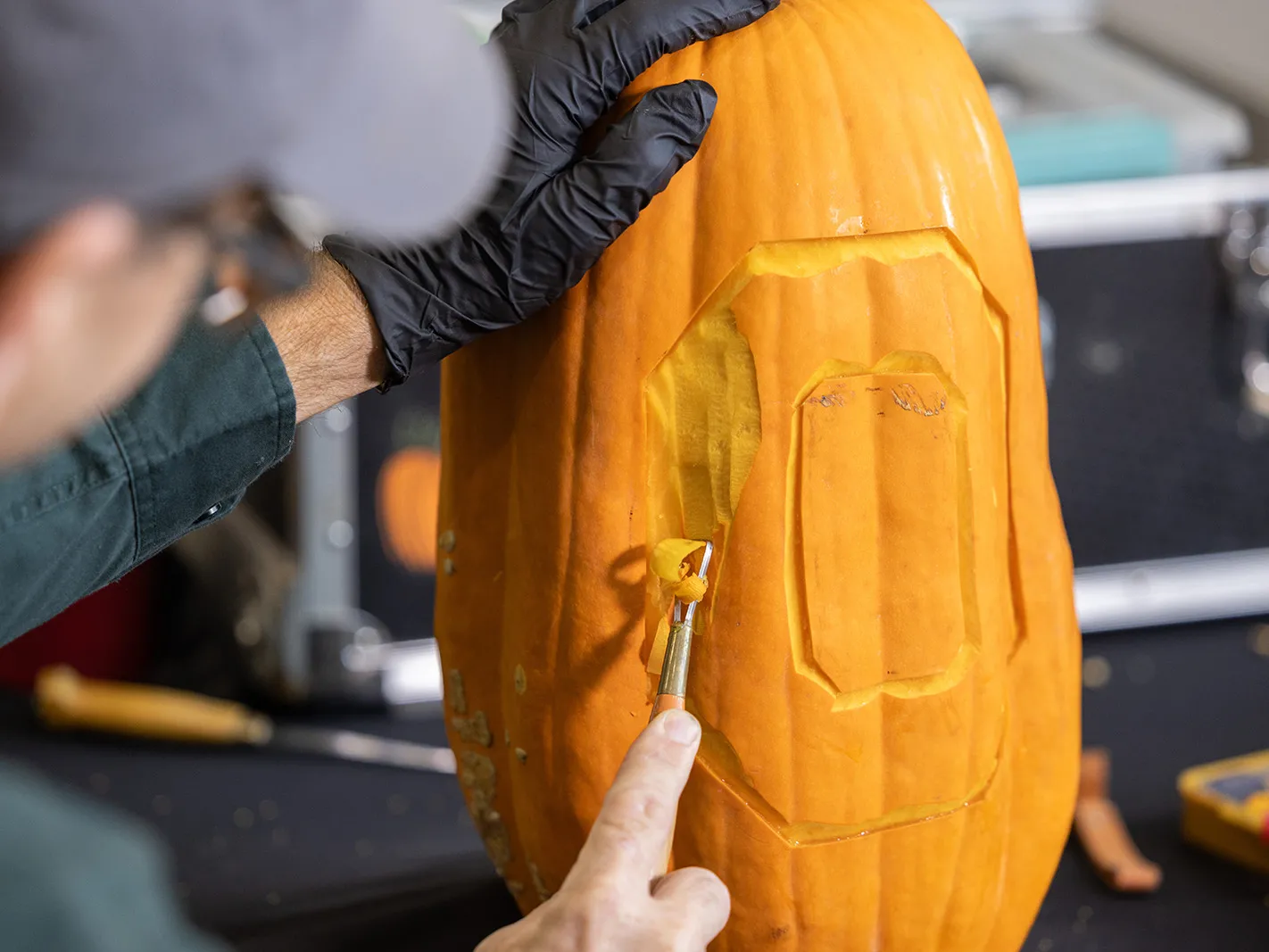 Gus uses a clay carving tool to remove the pumpkin skin between the lines he sliced out in the previous step.