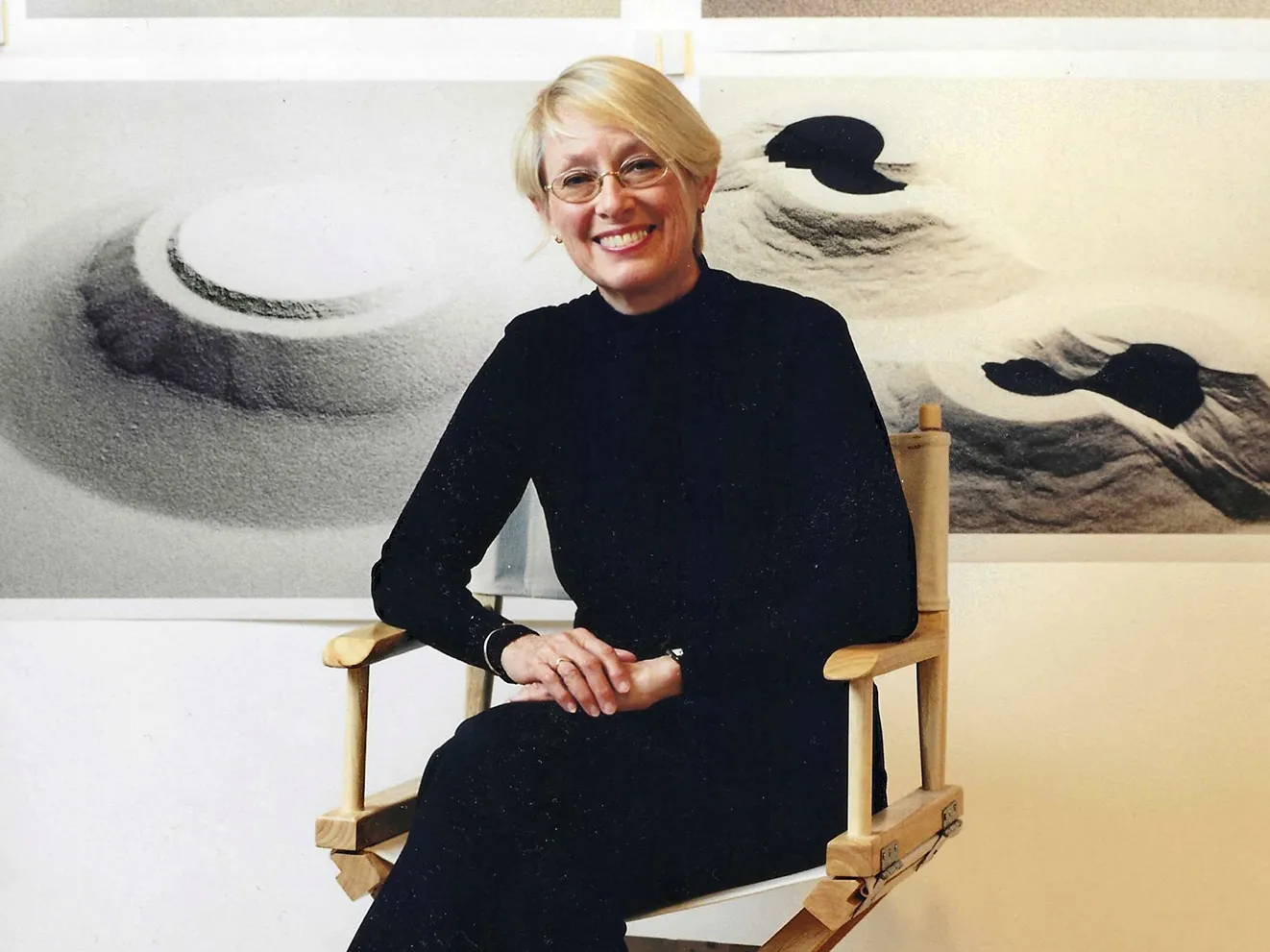 Connie Zehr, a white woman with short blond hair, oval glasses and a big smile, sits on a director&#039;s-style folding chair in front of photos of her works. They are all sand and they are mounded in different formations. They could be ancient or alien structures, or foot prints into mounded sand--they&#039;re abstract and so open to interpretation.