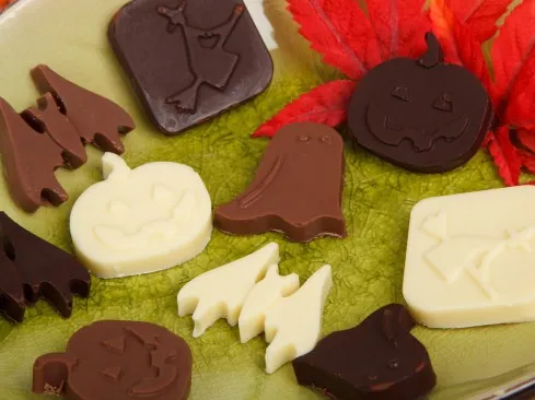 Sitting on a table are chocolates cut out in Halloween shapes like ghosts and pumpkins