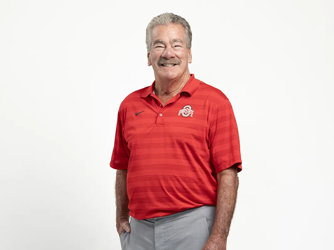 James “JT” Terranova grins for a portrait and stands with one hand tucked in a pocket and the other by his side. He wears an Ohio State golf shirt and dress pants, and is a white man with graying hair and a facial expression and smile so friendly, he could pass as a good Santa Claus actor, if you added long white hair and beard. Instead, he’s neatly trimmed.