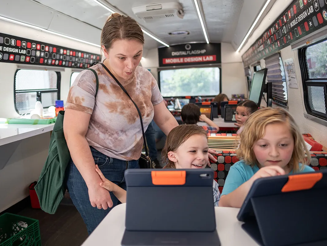 A mom oohs while her two children each sit in front of an iPad inside the STEM bus