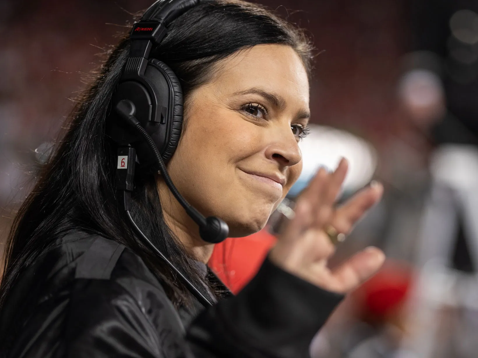Melissa smiles as she waves to someone off camera in this closeup photo of her. She wears a headset to talk to other coordinators.