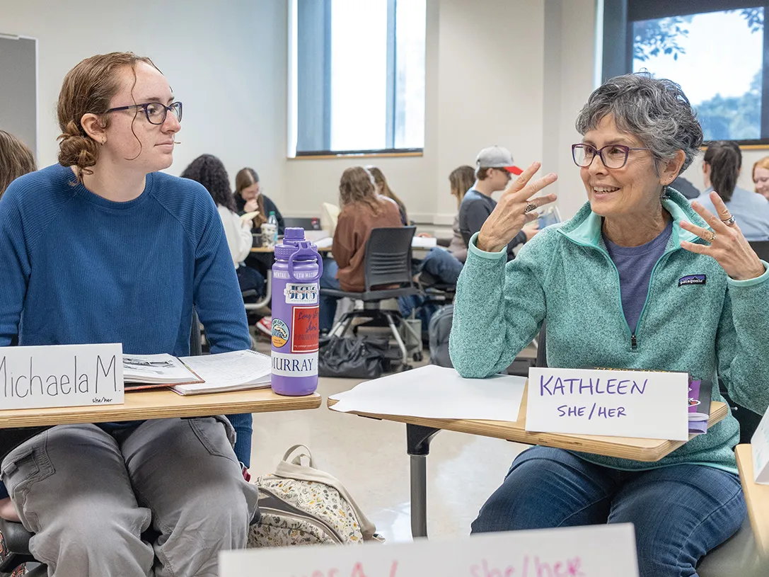 An older woman with short gray hair gestures as she makes a point while a young woman of traditional college student age listens during a small group discussion inside an Ohio State classroom.