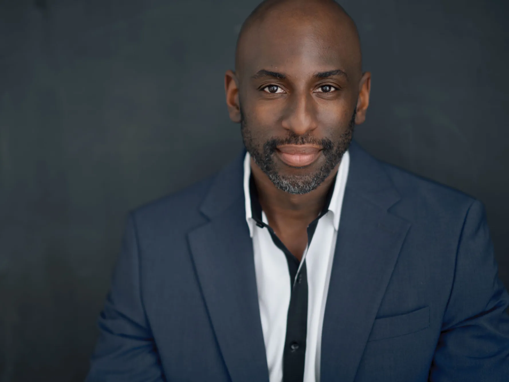 Rashad Chambers poses for a portrait wearing a suit and button down shift. A young-ish black man, he appears stylish, calm, confident and proud.