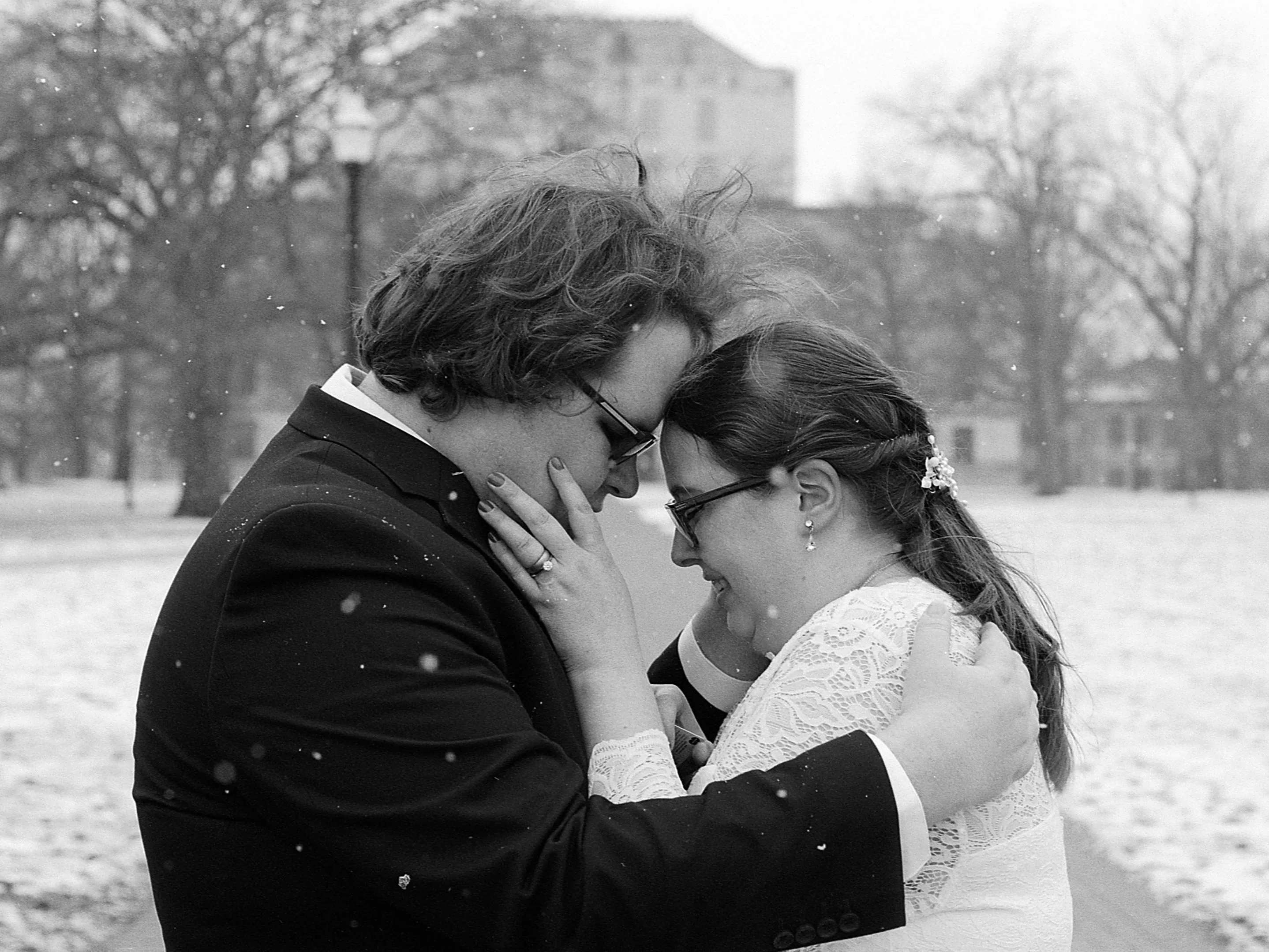 A bride and groom touch foreheads on The Oval as it snows in this black and white photo.
