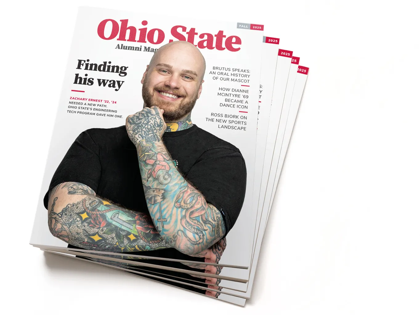 This is a stack of the fall 2025 edition of Ohio State Alumni Magazine. The cover shows alumnus Zachary Ernest sharing a friendly smile as he touches one hand to his chin. He wears a plain T-shirt, which sets off his blue eyes and colorful tattoos covering his arms and neck. Zack is a white man, in his early 30s, with shaved head and neat beard. 