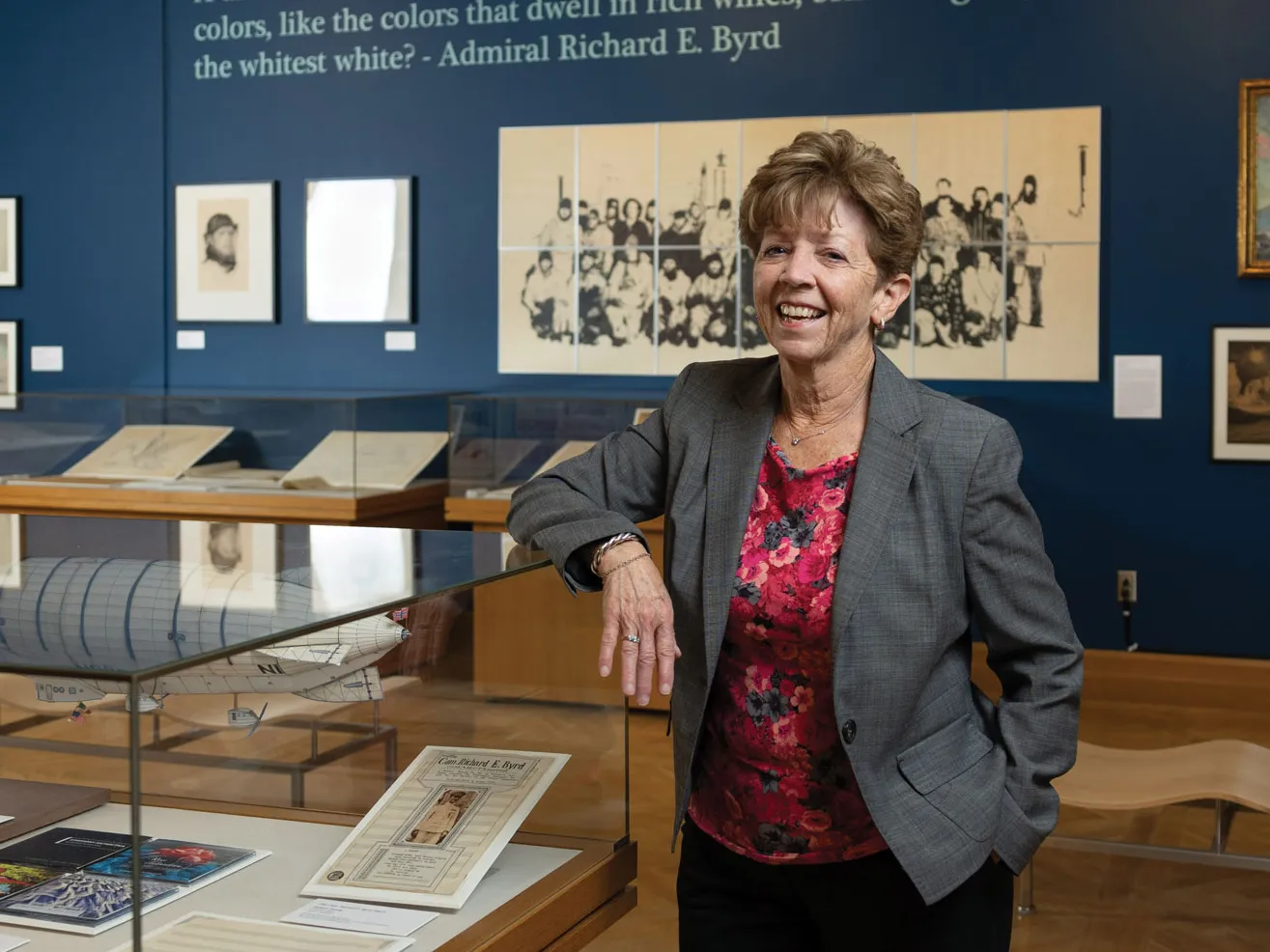 Laura Kissel stands in a museum exhibit she designed with polar artifacts. She’s laughing, wearing a suit coat and colorful shirt, and has an elbow propped on a glass display case. She looks like she’d be a fun co-worker.